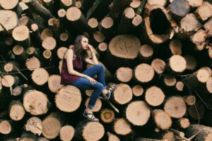 A young woman sitting on a pile of stacked logs, captured outdoors.